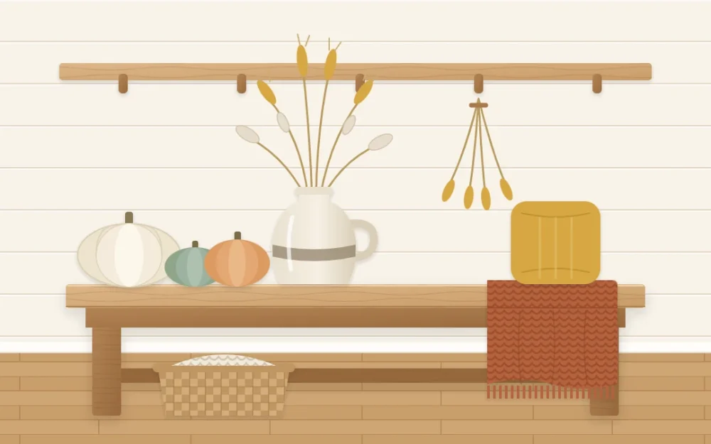 Farmhouse bench by a plank wall with cream, sage and soft orange pumpkins, a stoneware jug of dried grasses, a rust knitted throw and a mustard cushion