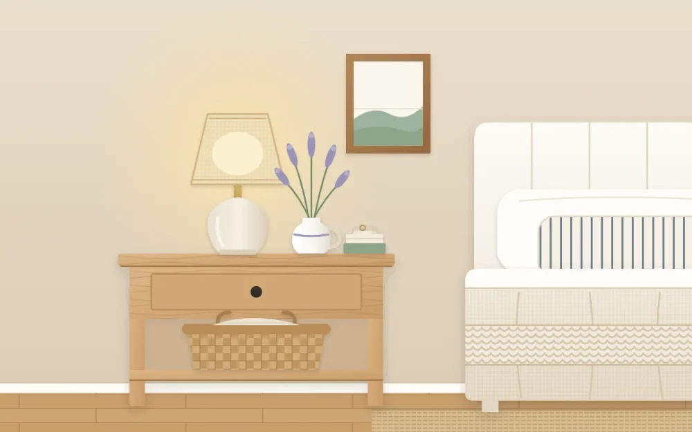 Wooden nightstand beside a linen-covered bed with a small ceramic lamp, a jug of stems, two stacked books, a dish and a basket below